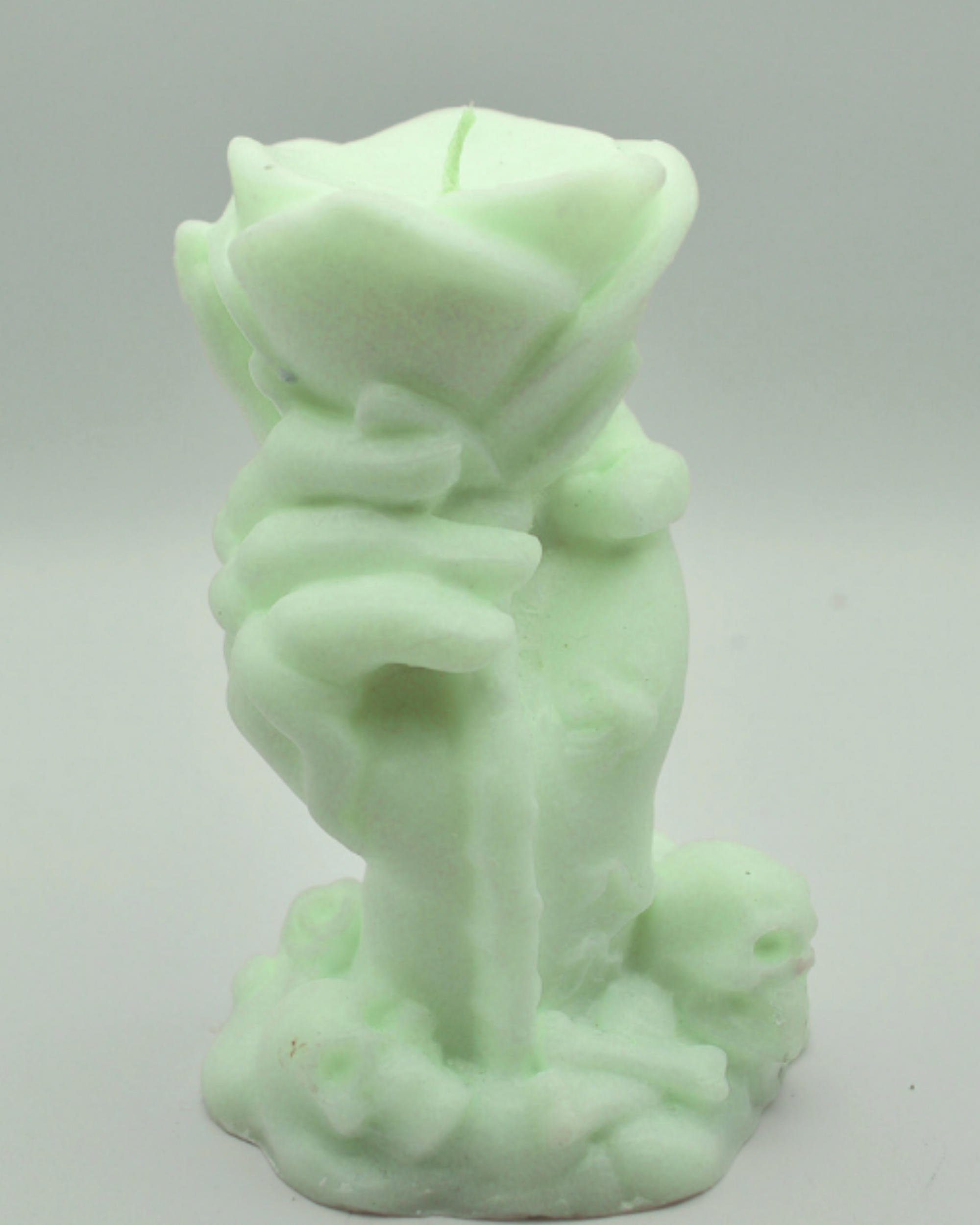 Mint green candle in the shape of a hand holding a rose on a light gray background