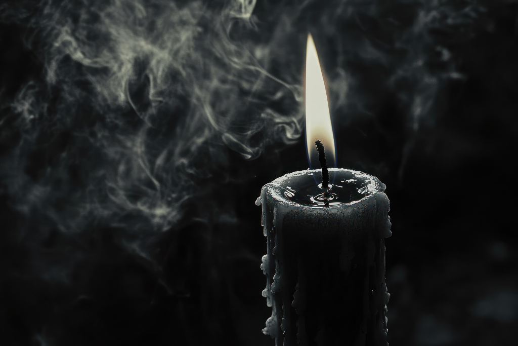 Black candle with a small flame against a dark background