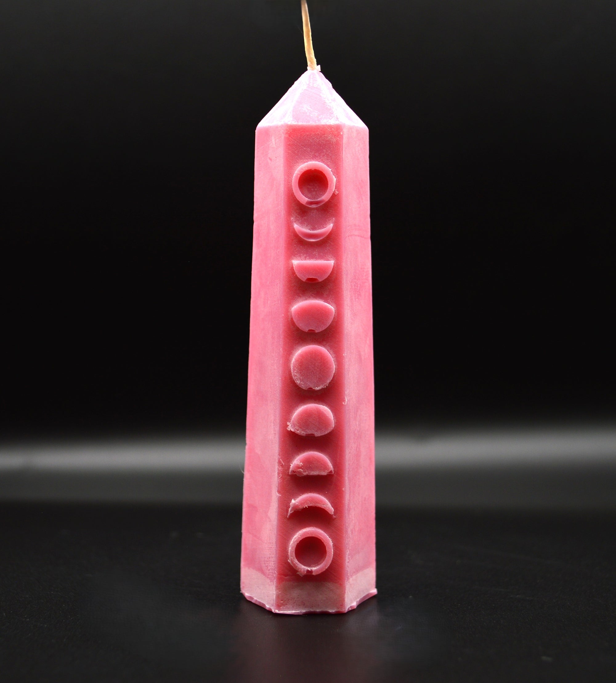 Pink candle with moon phases design on a black background
