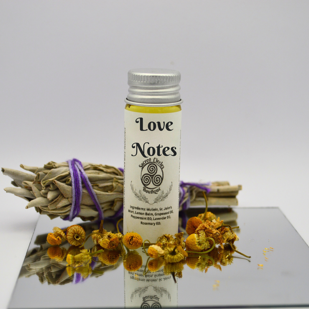 Love Notes body oil in 15 mL with dried flowers and herbs on a reflective surface
