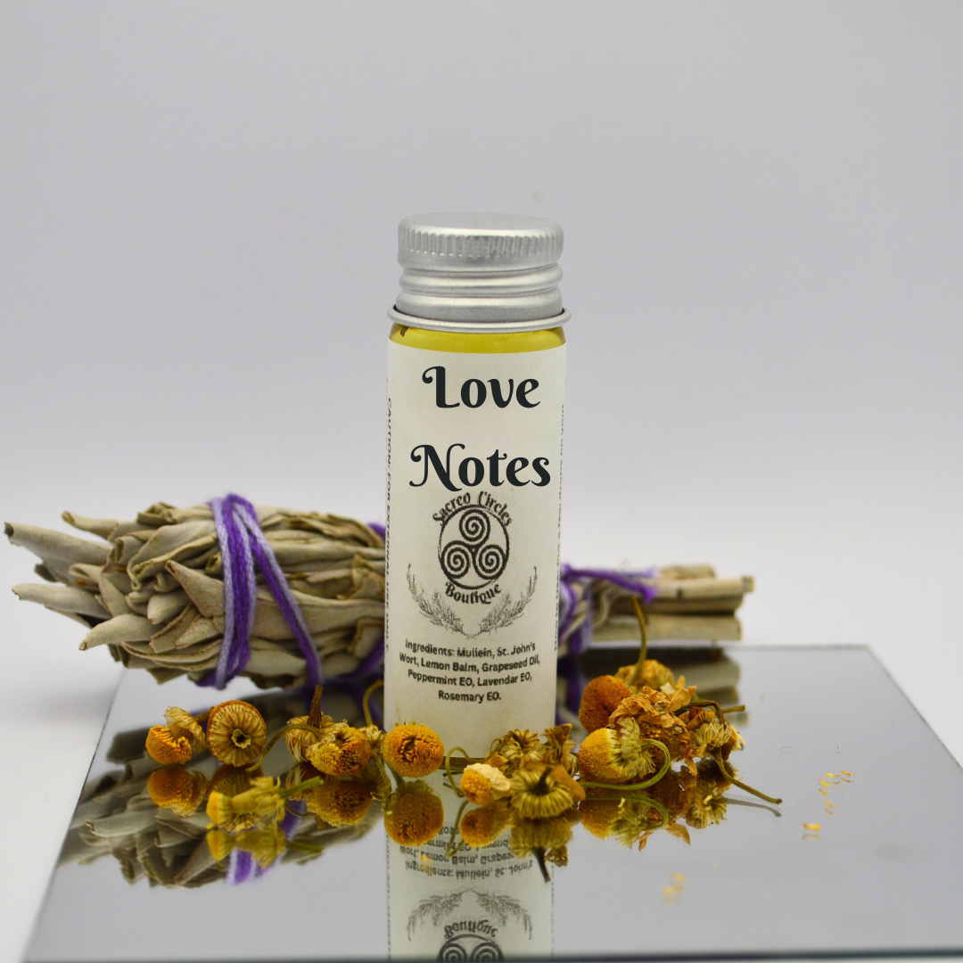 Love Notes body oil in 15 mL with dried flowers and herbs on a reflective surface
